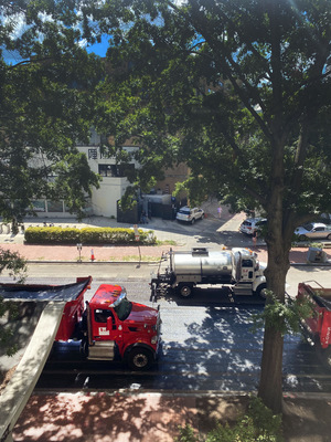 The silver truck is spraying the oil. The red trucks are full of new asphalt and staged for the next step.