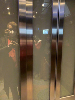 The elevator has opaque window panels, and you can see the building pass behind them.
